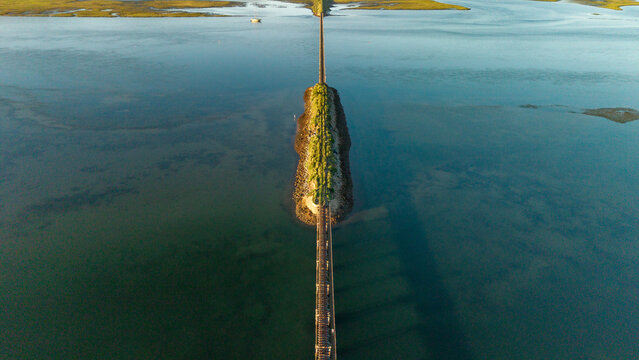 Aerial view of a narrow strip of land bisecting the tranquil lagoon, connected by a weathered bridge under a serene sky, Knysna, Western Cape, South Africa.