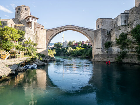 Bosnia and Herzegovina 05 28 2025: Frontal drone photo of Old Bridge Mostar in Old Town with Halebija Tower, Sultan Selimov Mesdžid, Koski Mehmed Pasha Mosque, blue Neretva River, boats, and beach