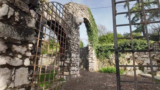 Walking through the old stone arch into Trsat&rsquo;s walled park, following the footpath toward the castle entrance with views opening toward the city and the Adriatic in the distance.