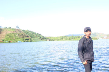 Naklejka premium Young man standing by large lake near terraced hillside agriculture landscape