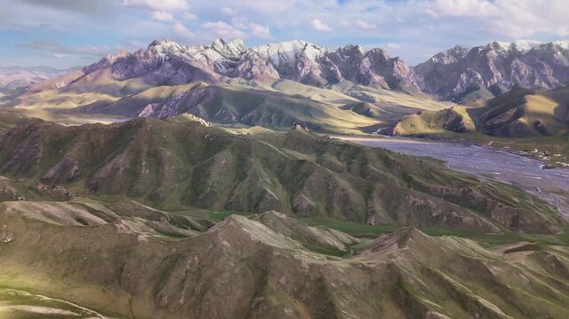 Aerial view over Kok-Kiya Valley, braided river and green hills below snow-capped Tian Shan mountains, Kyrgyzstan