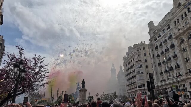 Crowd watches colorful smoke and explosions at Las Fallas festival in Plaza del Ayuntamiento, Valencia
