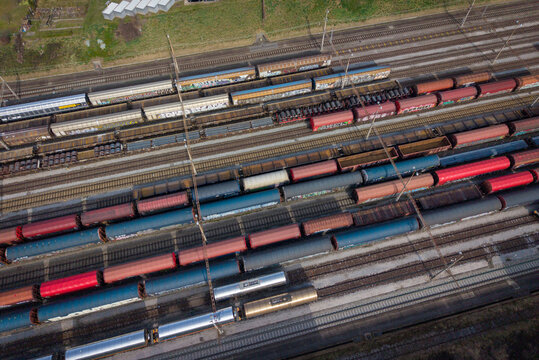 Aerial view of a sprawling tapestry of rail lines hosting a diverse collection of colorful freight cars, creating a vibrant mosaic of industrial transport, Chiasso, Ticino, Switzerland.