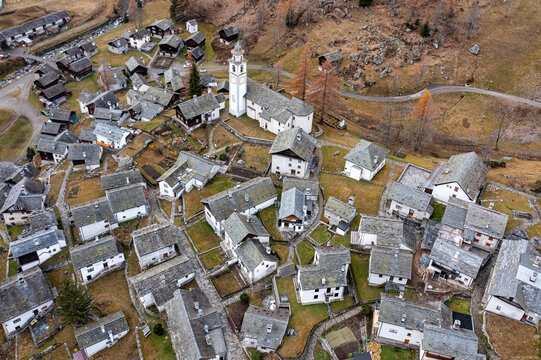 Aerial view of stone Walser houses clustered together under a muted sky, dominated by the church's white spire, creating a timeless scene, Bosco Gurin, Ticino, Switzerland.