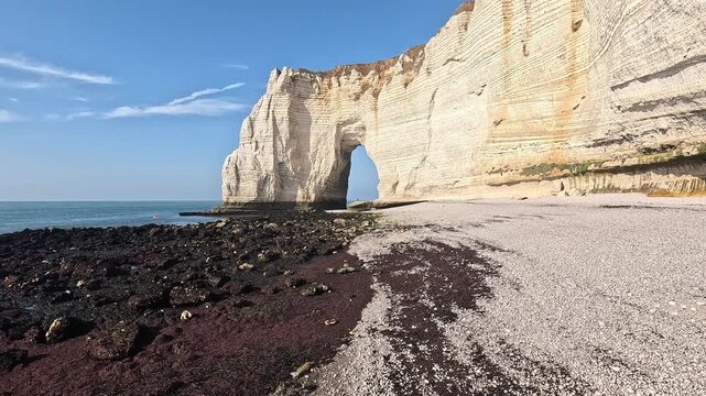 Wide view of Etretat natural limestone arch and pebble beach beneath towering chalk cliffs, Normandy coastline, France