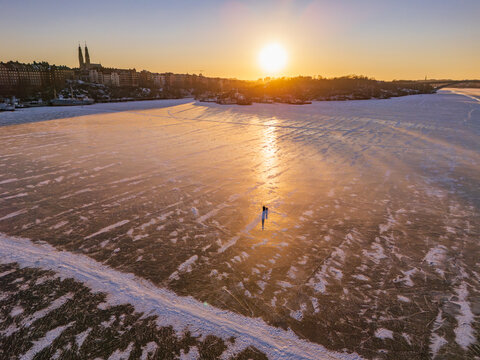 Aerial view of a solitary figure glides across the vast expanse of cracked ice under the warm glow of the setting sun near Norr Malarstrand, Stockholm, Stockholms lan, Sweden.