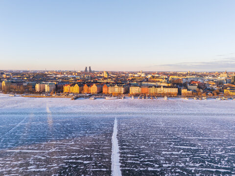 Aerial view of the sun casting a golden glow over the city skyline contrasting with the icy expanse of the frozen lake, Stockholm, Stockholms lan, Sweden.