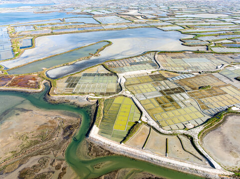 Aerial view of the intricate patchwork of salt marshes reflecting the sky, divided by earthworks and waterways, a testament to human cultivation and nature's artistry, Guerande, Bretagne, France.