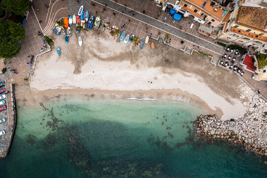 Aerial view of boats clustered like vibrant jewels along the shore, contrasting with the soft beach and the deep blue sea, Cetara, Campania, Italy.