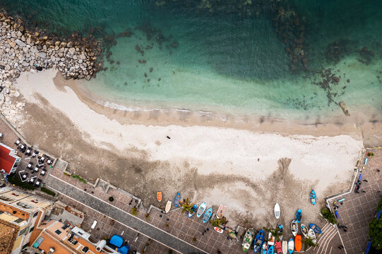 Aerial view of the sandy beach kissing the turquoise waters, framed by colorful boats and buildings along the coastline, Cetara, Campania, Italy.