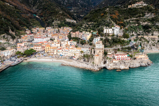 Aerial view of vibrant buildings cascading down to the turquoise sea, where a historic tower stands guard over the rocky coastline, Cetara, Campania, Italy.