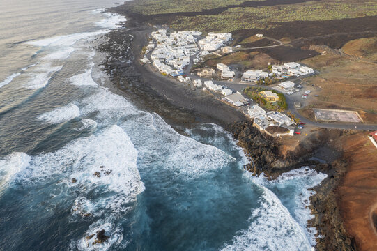 Aerial view of the whitewashed village nestled between black volcanic rocks and the turquoise ocean, a striking contrast of colors and textures, El Golfo, Canary Islands, Spain.