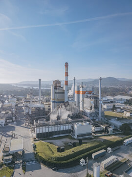 Aerial view of the DS Smith paper mill industrial facility with tall chimneys piercing the clear blue sky, contrasting with the surrounding green landscape, Deocriste, Portugal.