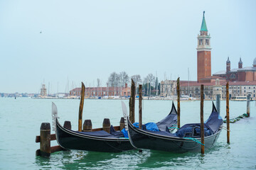 Obraz premium Row of gondolas moored on lagoon in foggy morning in Venice with San Giorgio Maggiore island in background