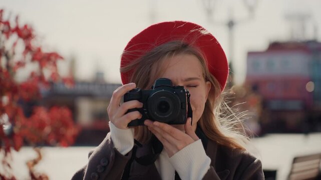 Young woman holding camera close, brings lens to eye and captures candid portraits with bokehfilled background, shutter action, creative focus, urban autumn scene and hobbyist photographer energy.