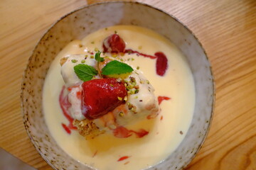 Creamy custard with soft cake pieces, fresh strawberries, mint leaf, and crushed pistachios, presented in a bowl. © vannet