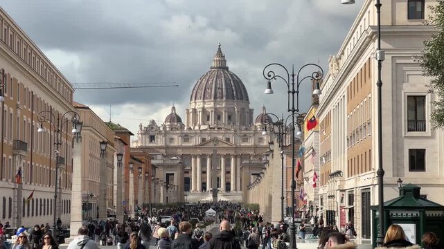 Scenic view of St. Peter&rsquo;s Basilica dome in Vatican City framed by Roman street, vintage lampposts and umbrella pine trees under dramatic cloudy sky.