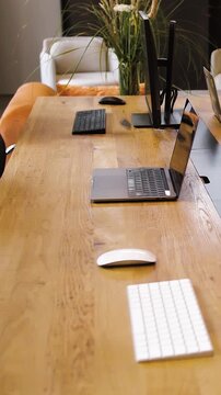 Vertical video. Wooden table with laptop and white keyboard. Loft style office with open space without people. Video of modern office.