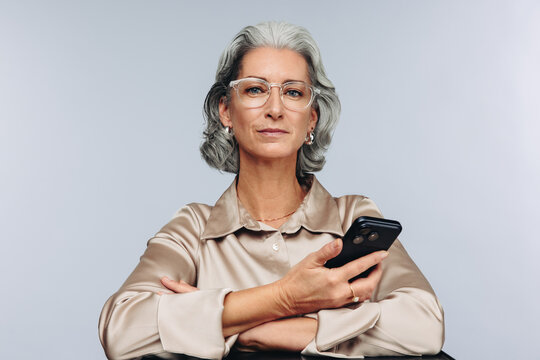 Mature woman crosses arms holding smartphone
