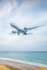 Obraz premium Skyline view of an airplane flying over a beach with ocean waves and distant clouds during day light hours