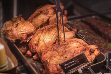 Grilled chicken Rotisserie, with a golden brown crust, cooked entirely on a spit, lies on the counter in close-up. Chickens are presented in the showcase of a restaurant or the ready-to-eat department