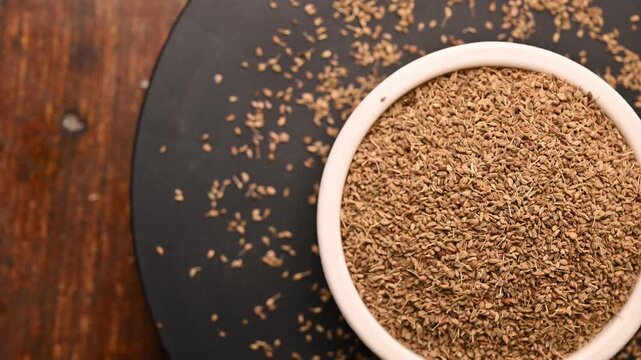 Top View of Carom Seeds (Ajwain) in White Bowl on Black Background &ndash; Rotating Footage