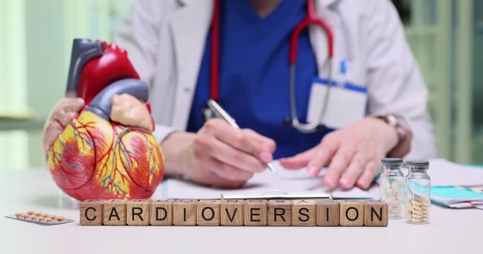 Woman cardiologist carefully studies test results of patient. Wooden cubes form word Cardioversion indicating medical procedure under consideration