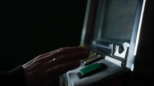 A gambler plays a retro slot machine, inserting a coin and pressing the Start button. The man hand presses the button and celebrates his victory. Slow motion.