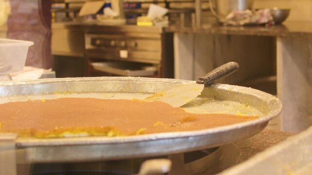 Close up kunafa dessert being served in paper plate with hot sugar syrup poured from metal bowl street sweets shop food preparation close up