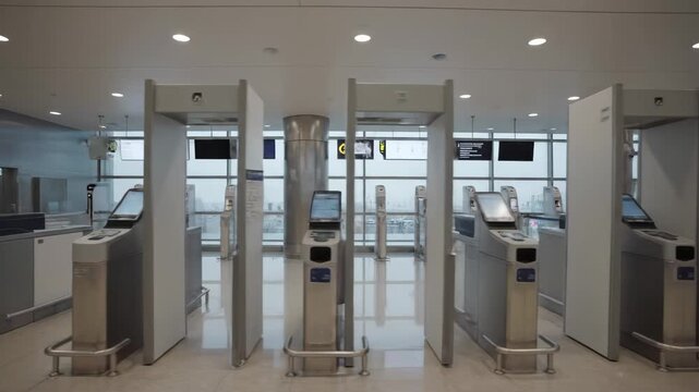 A wide shot of a modern, empty airport security checkpoint featuring automated gates, self-service kiosks, and metal detectors.