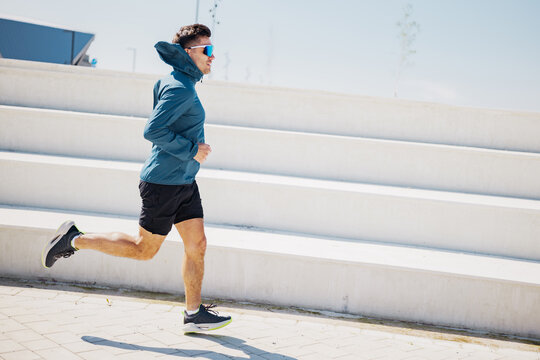 Man runs on outdoor stairs in sunny weather wearing a jacket and shorts in the daytime