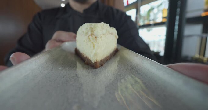A slice of cheesecake is on a white plate. The plate is being held by a person