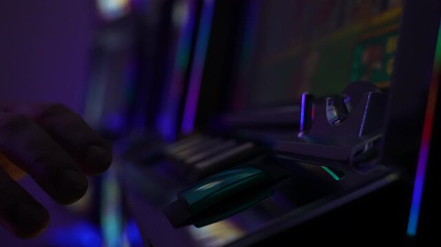 Dramatic close up of a player hand pressing the green start button on an old slot machine in a dark casino interior. Slow motion.