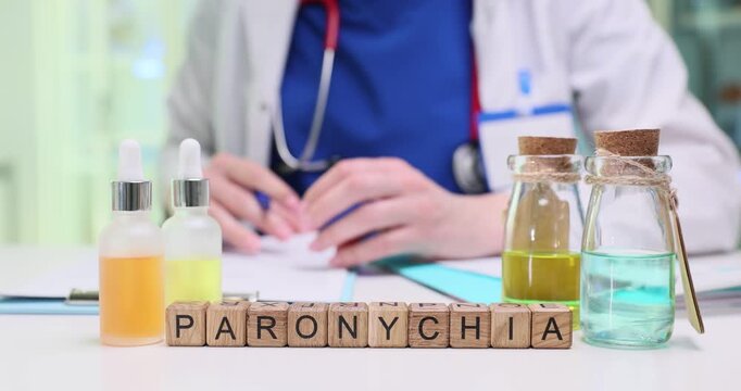 Wooden cubes on table form word Paronychia indicating suspected medical condition. Woman doctor reviews medical history of patient near medicines