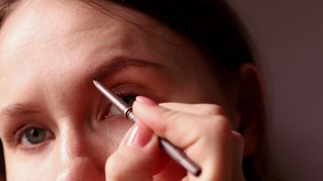 Close up of a young woman using a fine-tip professional makeup brush to define and fill in her eyebrows. Detailed view of eyebrow styling and facial grooming routine