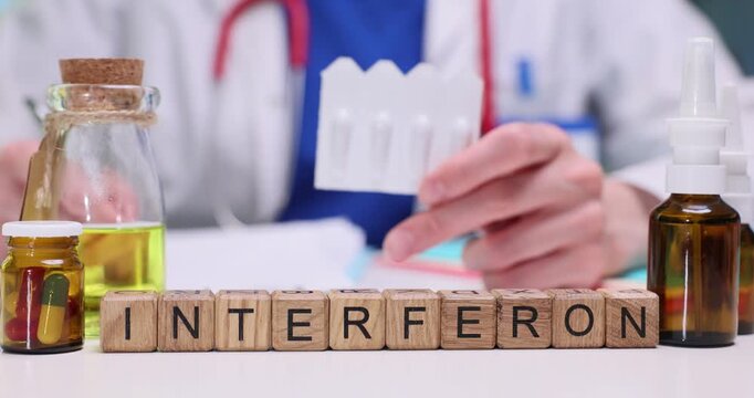 Miniature wooden cubes form word Interferon on table. Experienced woman physician shows medical suppositories and explains purpose to patient
