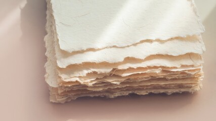 Fototapeta premium Stacked sheets of handmade paper with visible fiber strands and a soft pastel background showing subtle light and shadow details