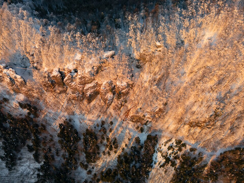 Aerial view of snow-dusted trees and rocky outcrops bask in the soft glow of sunlight, casting long shadows across the winter landscape, Kremnicke vrchy, Banska Bystrica Region, Slovakia.