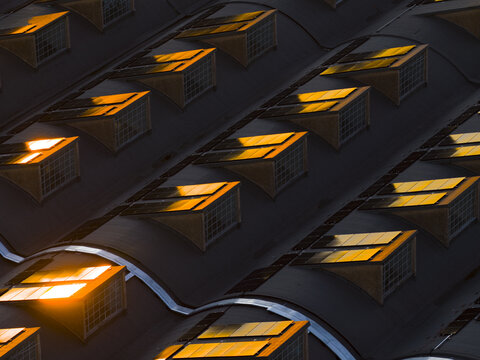Aerial view of geometric patterns of rooftop windows reflecting golden light, creating a warm glow against the cool shadows, Roma, Lazio, Italy.