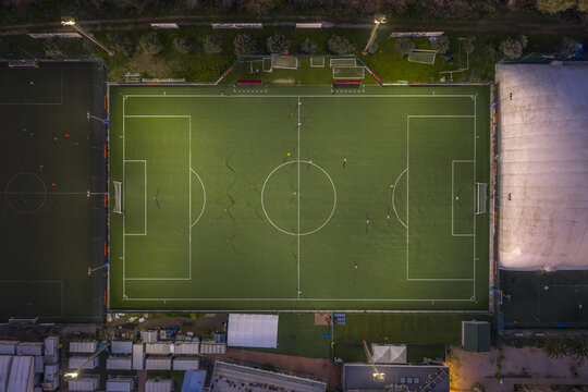 Aerial view of the illuminated football field with its bright green turf amidst the darker surroundings, 8 Piazzale dei Santi Pietro e Paolo, Roma, Lazio, Italy.