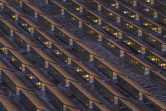 Aerial view of geometric patterns of building facade with rows of windows reflecting warm interior light, Lazio, Italy.