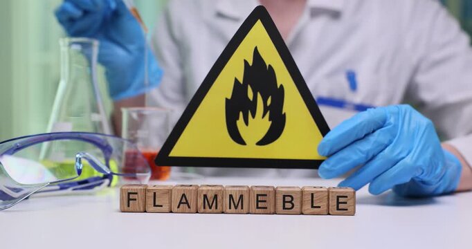 Miniature wooden cubes on laboratory table form word Flammable. Chemist clearly shows warning sign indicating serious risk of liquids ignition