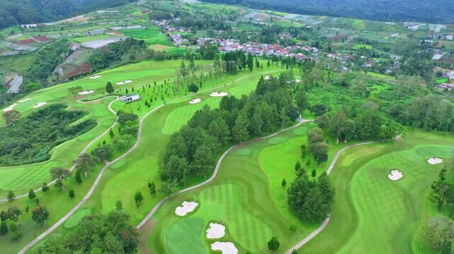 Drone footage of large golf course with winding fairways and sand bunkers near suburban neighborhood.