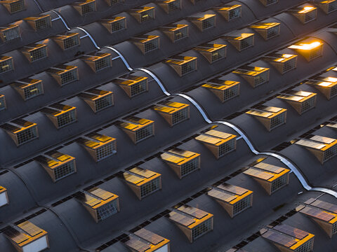 Aerial view of a building's rooftop with geometric windows catching the fading sunlight, creating a mesmerizing pattern of light and shadow, Roma, Lazio, Italy.