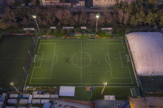 Aerial view of the illuminated football field casting a vibrant green glow against the dark surroundings, Roma, Lazio, Italy.