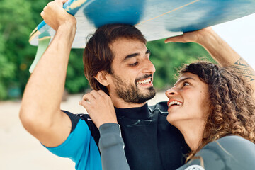 Portrait of a young couple surfing at the beach, holding surfboards, having fun together ocean...