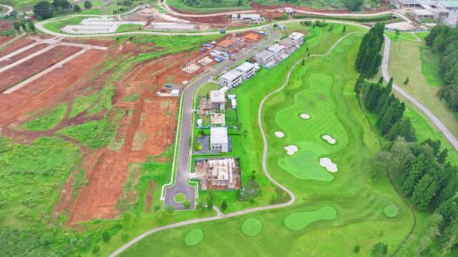 Drone footage of green golf course with sand bunkers next to residential buildings and construction land.