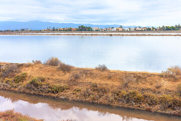 Obraz premium Scenic view shows the Molentargius Saline Regional Park in Cagliari, Italy. Historic salt ponds and wetlands sit before a distant skyline and mountains under cloudy sky