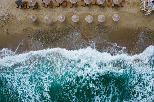 Aerial view of the beach where the turquoise waves crash against the shore, umbrellas line the sandy coast, Chania, Chania, Greece.