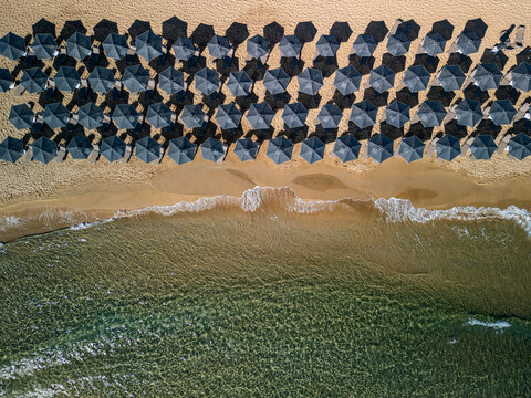 Aerial view of dark umbrellas contrast with the golden sand where gentle waves caress the shore, creating a serene coastal scene, Chania, Chania, Greece.
